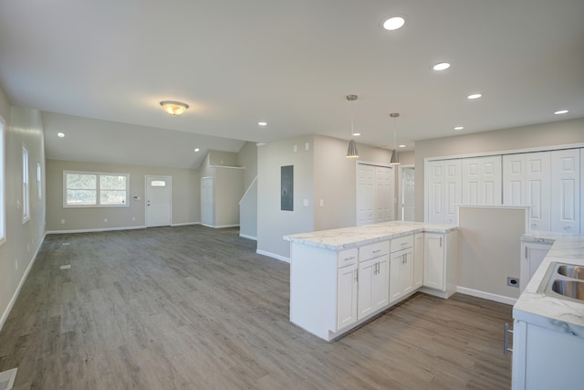 kitchen featuring electric panel, light wood-type flooring, hanging light fixtures, and white cabinetry