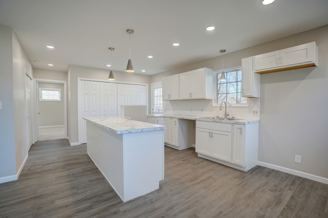 kitchen featuring white cabinetry, a center island, wood finished floors, and a sink