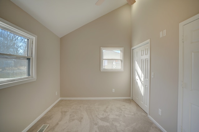 empty room featuring light carpet, visible vents, high vaulted ceiling, and baseboards