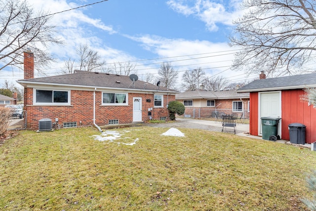 back of property featuring brick siding, a yard, central AC unit, fence, and an outdoor structure