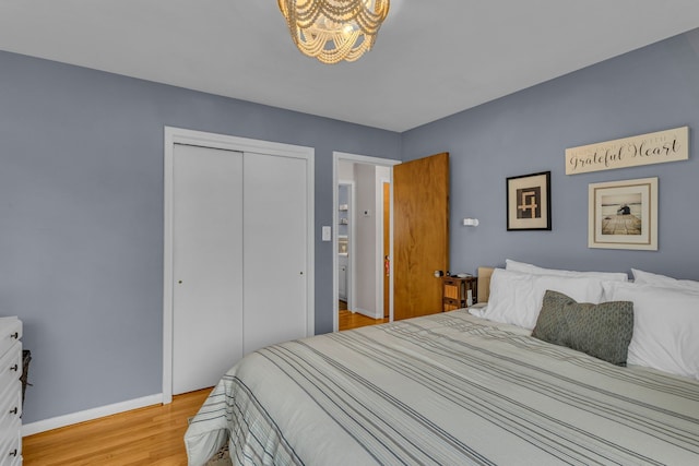 bedroom featuring a closet, light wood-style flooring, baseboards, and an inviting chandelier