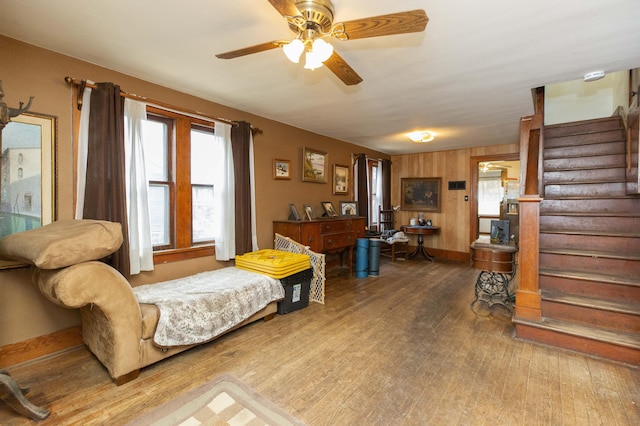 living area with a ceiling fan, stairway, baseboards, and wood finished floors