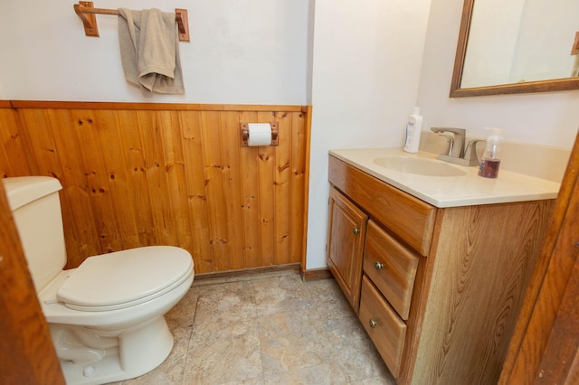 half bath with wainscoting, wood walls, vanity, and toilet