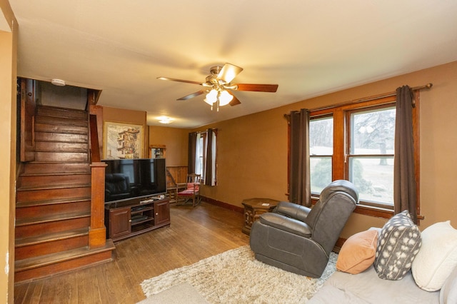 living room featuring dark wood-style floors, stairs, baseboards, and a ceiling fan