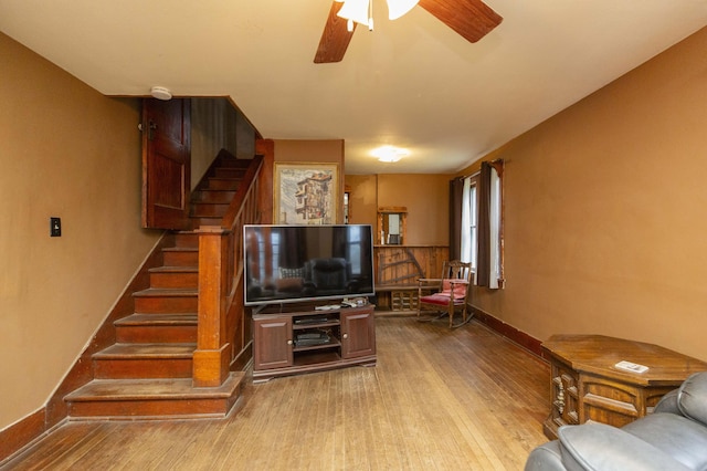 living area featuring a ceiling fan, stairway, baseboards, and wood finished floors