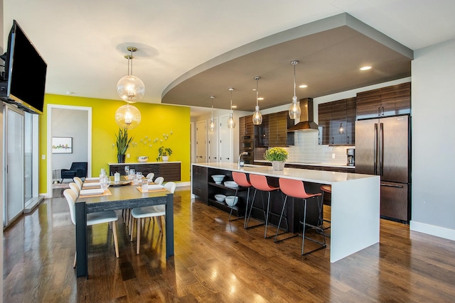 kitchen featuring light countertops, appliances with stainless steel finishes, wall chimney range hood, dark wood-style floors, and modern cabinets