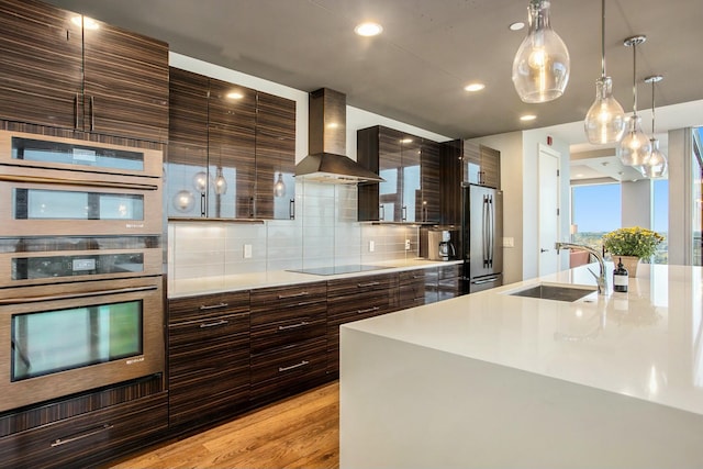 kitchen with decorative backsplash, appliances with stainless steel finishes, light countertops, wall chimney range hood, and a sink