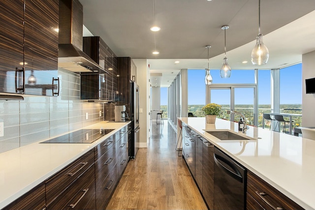 kitchen featuring dishwashing machine, black electric stovetop, a sink, wall chimney range hood, and modern cabinets