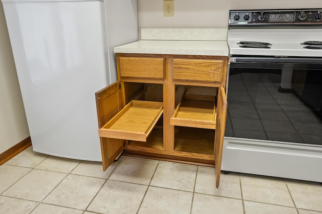 room details featuring range with electric stovetop, baseboards, light countertops, freestanding refrigerator, and brown cabinets