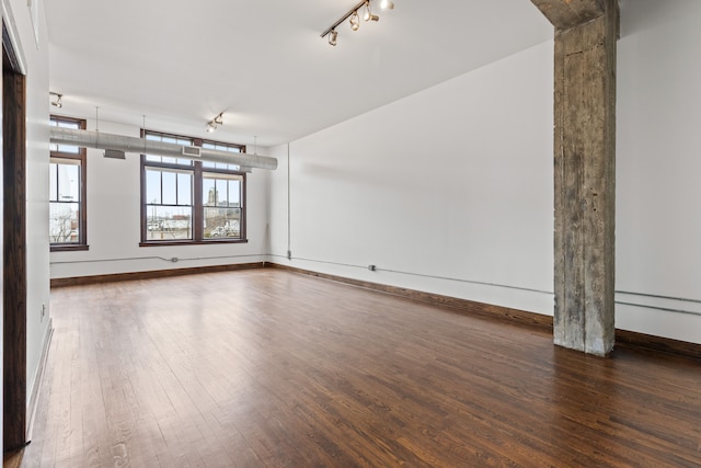 unfurnished room featuring baseboards, wood finished floors, and track lighting