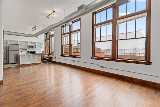 unfurnished living room with plenty of natural light, dark wood finished floors, visible vents, and rail lighting