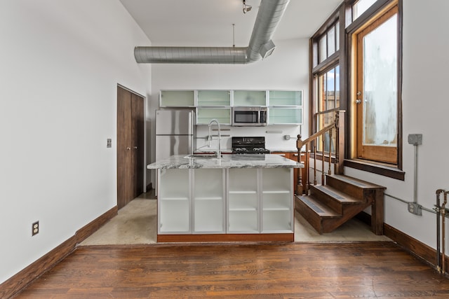 kitchen featuring light stone counters, dark wood finished floors, stainless steel appliances, glass insert cabinets, and baseboards