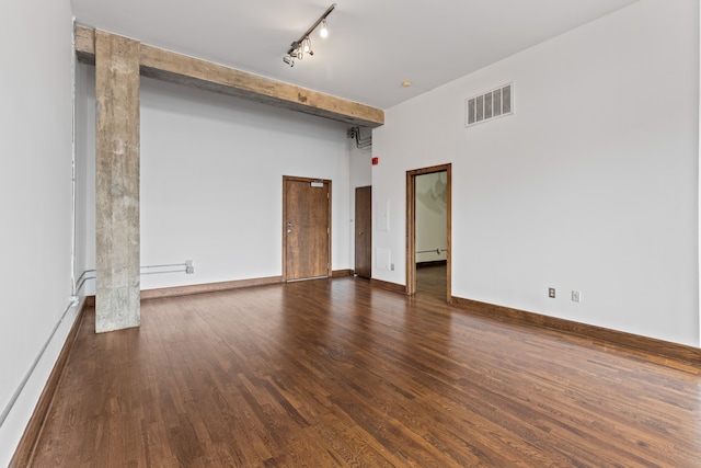 spare room with dark wood-style flooring, visible vents, baseboards, beamed ceiling, and rail lighting