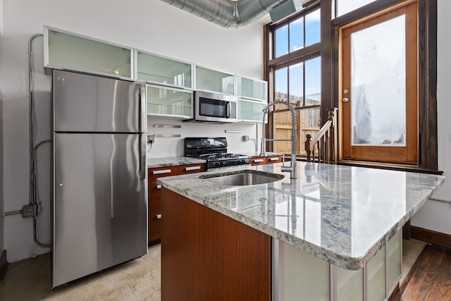 kitchen featuring stainless steel appliances, a sink, glass insert cabinets, and light stone counters