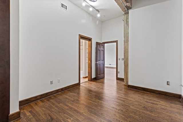 empty room featuring visible vents, baseboards, a towering ceiling, wood finished floors, and track lighting