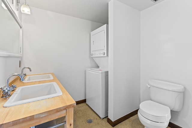 interior space featuring stacked washer / dryer, laundry area, a sink, and baseboards