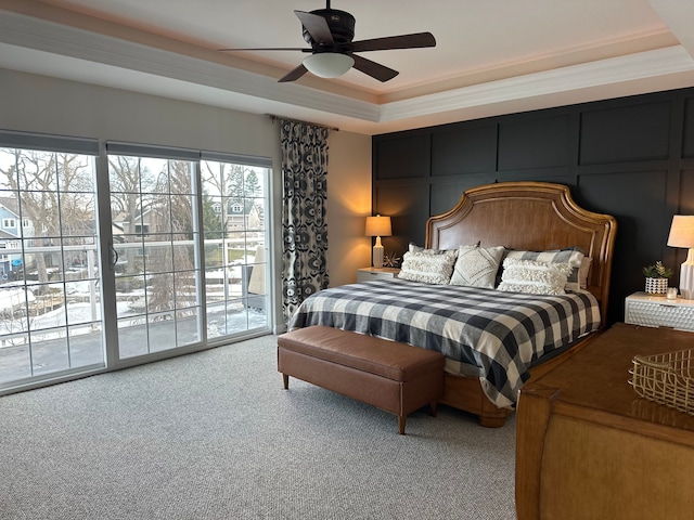 carpeted bedroom featuring a raised ceiling, ceiling fan, access to outside, crown molding, and a decorative wall