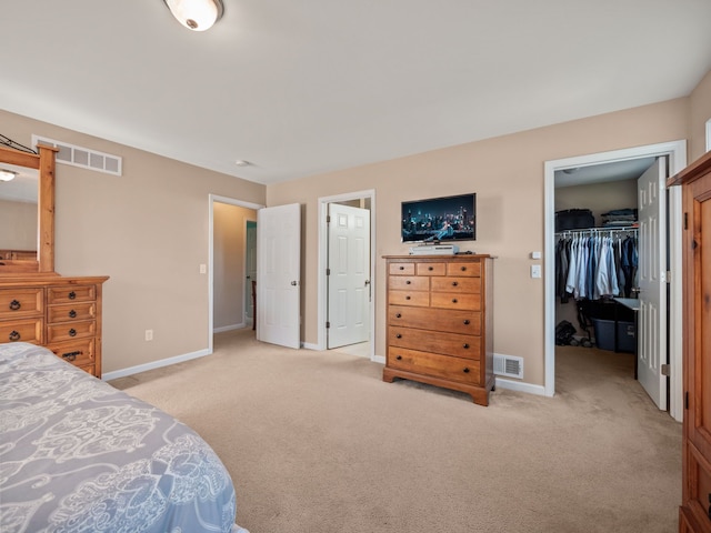 bedroom with visible vents, baseboards, light colored carpet, a walk in closet, and a closet