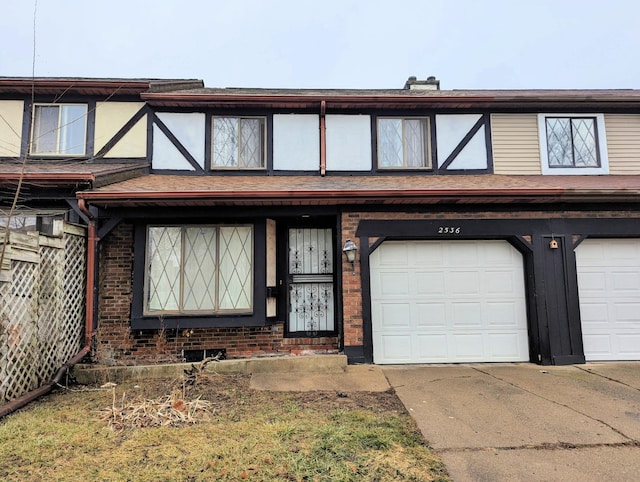 tudor home featuring a garage, concrete driveway, brick siding, and roof with shingles