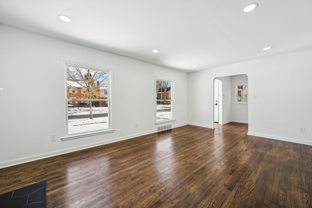 unfurnished living room with arched walkways, recessed lighting, dark wood-style flooring, visible vents, and baseboards