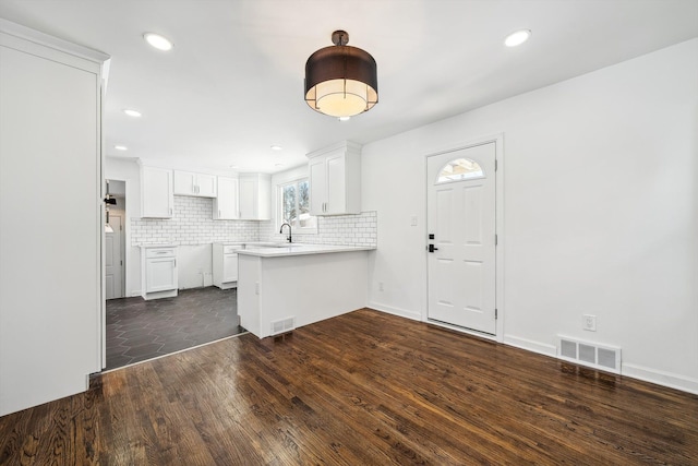 kitchen featuring white cabinets, visible vents, a peninsula, and decorative backsplash