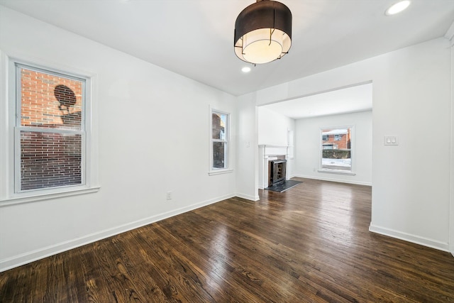 unfurnished living room featuring baseboards, a fireplace with raised hearth, dark wood-style flooring, and recessed lighting