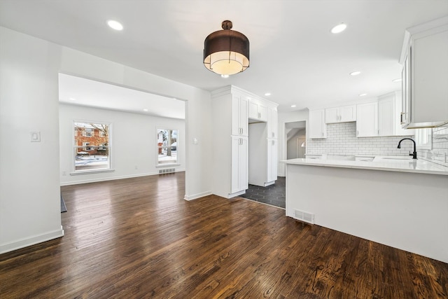 kitchen featuring dark wood-style floors, light countertops, visible vents, backsplash, and a peninsula