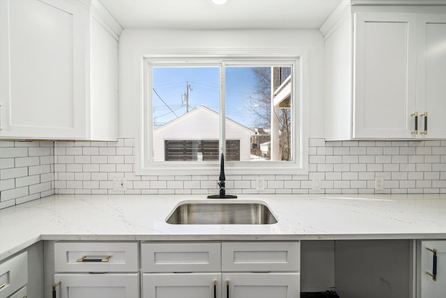 kitchen with light stone countertops, a sink, white cabinetry, and decorative backsplash