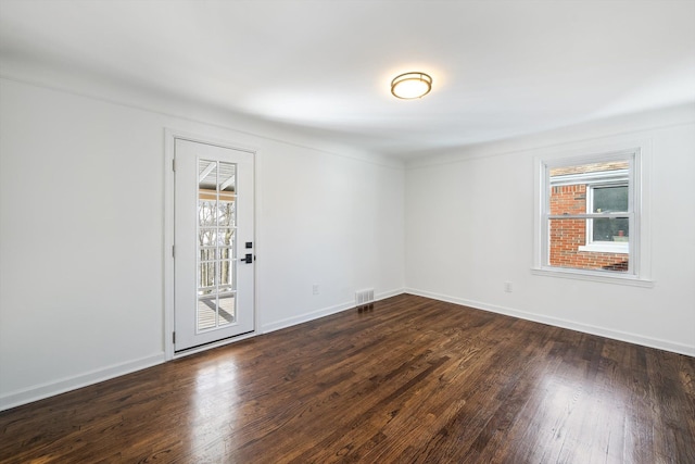 unfurnished room with visible vents, dark wood finished floors, and baseboards