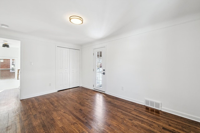 spare room featuring a healthy amount of sunlight, dark wood-style flooring, visible vents, and baseboards