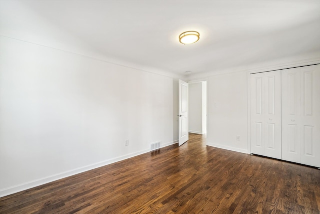 unfurnished bedroom with a closet, dark wood-style flooring, visible vents, and baseboards