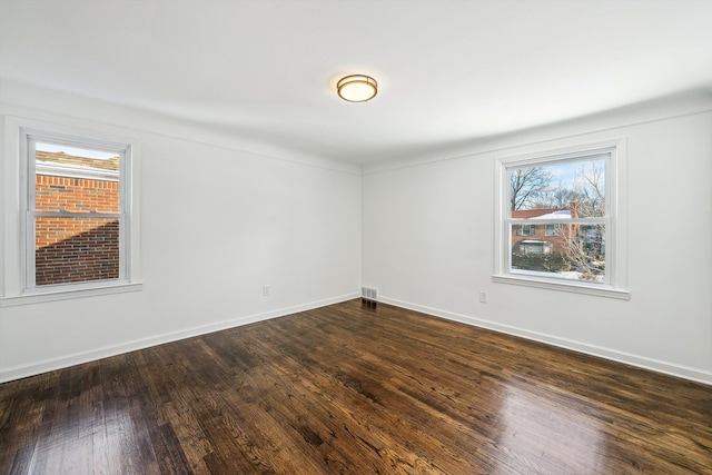 unfurnished room with visible vents, dark wood finished floors, and baseboards