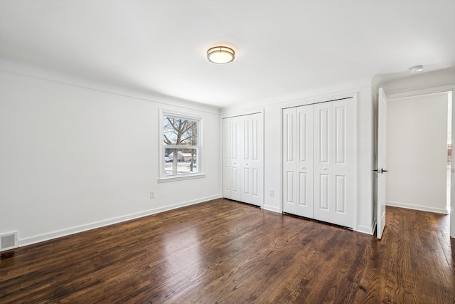 unfurnished bedroom with multiple closets, dark wood finished floors, and baseboards