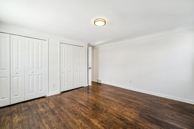 unfurnished bedroom featuring baseboards, visible vents, dark wood-type flooring, and multiple closets