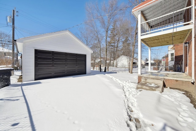 snowy yard with an outbuilding, a detached garage, and a balcony