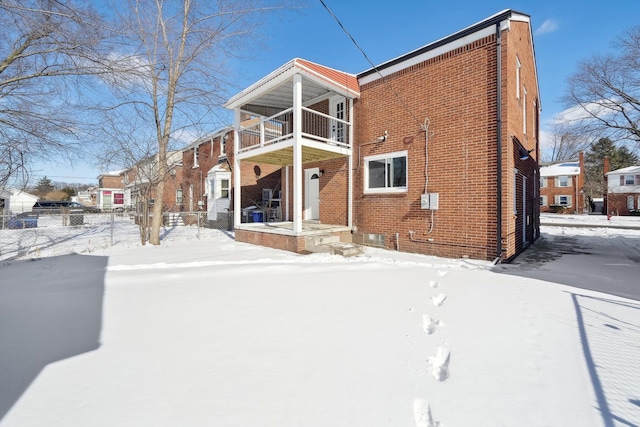 snow covered rear of property featuring brick siding and a balcony