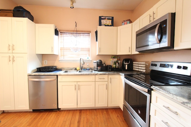 kitchen featuring stainless steel appliances, light wood-type flooring, a sink, and white cabinets