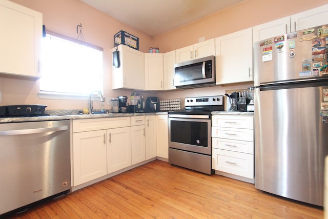 kitchen featuring light wood finished floors, appliances with stainless steel finishes, white cabinetry, a sink, and light stone countertops