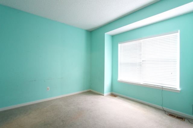 carpeted empty room with a textured ceiling, visible vents, and baseboards