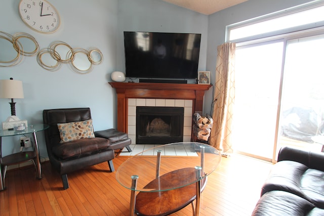 living room with lofted ceiling, hardwood / wood-style floors, and a tiled fireplace