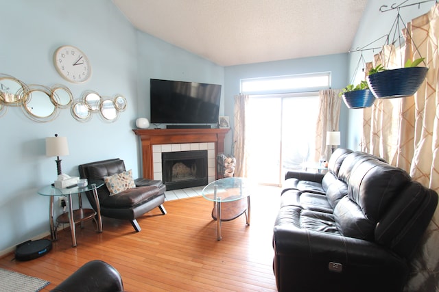 living room with a textured ceiling, wood-type flooring, baseboards, vaulted ceiling, and a tiled fireplace