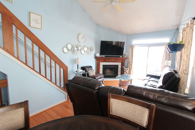 living area with high vaulted ceiling, a tile fireplace, wood finished floors, a ceiling fan, and stairway