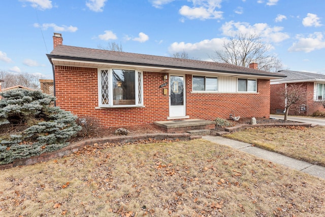 single story home featuring brick siding, a chimney, and a front yard