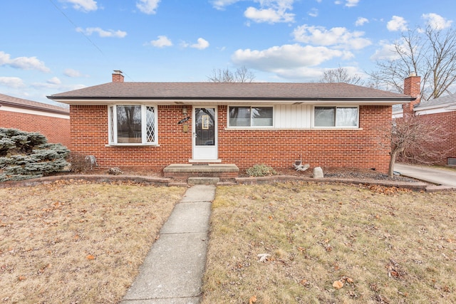 view of front of home featuring a shingled roof, a front yard, a chimney, and brick siding