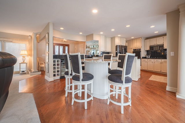 kitchen featuring a breakfast bar, a kitchen island, light wood-type flooring, black appliances, and ornate columns