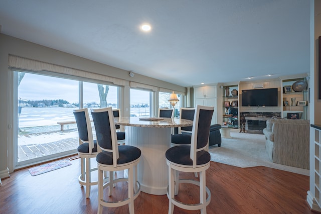 kitchen with a glass covered fireplace, wood finished floors, a kitchen island, white cabinets, and a kitchen bar