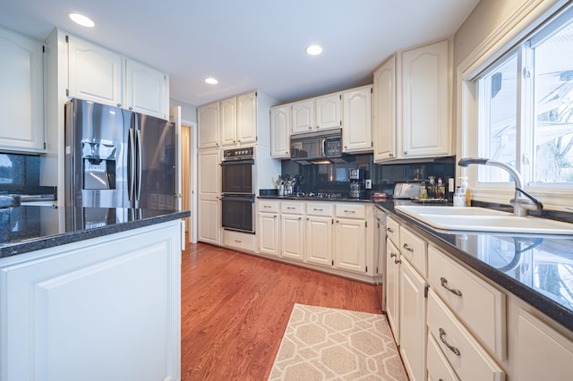 kitchen featuring tasteful backsplash, white cabinetry, a sink, light wood-type flooring, and black appliances