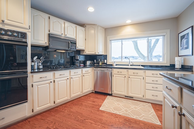 kitchen featuring black appliances, dark countertops, a sink, and light wood-style floors