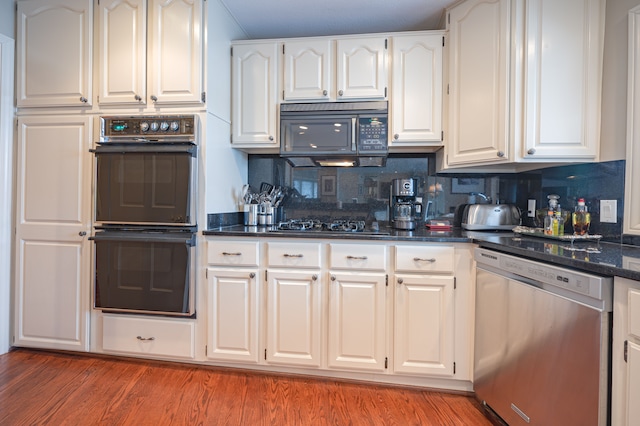 kitchen featuring tasteful backsplash, dark stone counters, white cabinets, light wood-style flooring, and black appliances