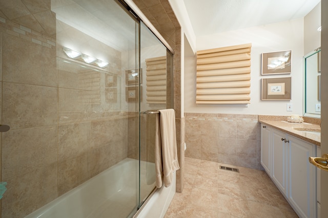 full bathroom featuring a wainscoted wall, shower / bath combination with glass door, vanity, visible vents, and tile walls